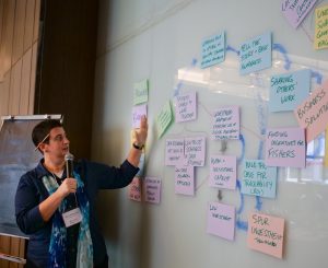 Lady pointing to a whiteboard with sticky notes covering it to capture the discussion